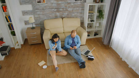 Top view of caucasian couple in denim browsing on smartphone on the floor of their apartmentの写真素材