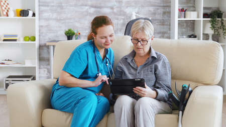 Female nuse helping senior elderly retired woman how to use her tablet computer in nursing homeの写真素材