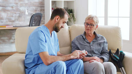 Male nurse sitting on couch with senior woman giving her medical treatment in nursing home.の写真素材