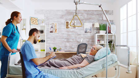 Team of male and female nurses checking an old lady lying in hospital bed in a retirement homeの写真素材