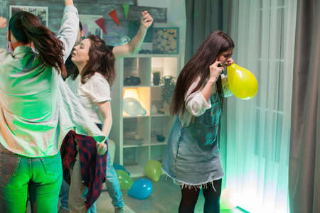 Beautiful young woman holding a balloon while having a conversation on her phone at a party with loud music.の写真素材