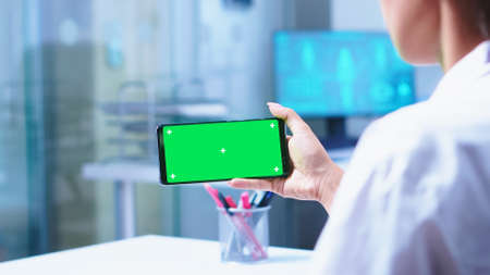 Medical nurse opening glass door of hospital cabinet and doctor using smartphone with green screen.の写真素材