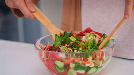 Woman mixing salad with wooden spoons for healthy meal in kitchen.の写真素材