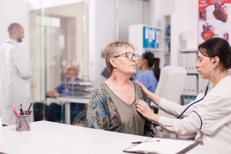 Doctor listening senior woman heart beat with stethoscope in hospital office wearing white coat.