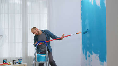 Guy singing during home repair using roller brush dipped in blue paint.の写真素材