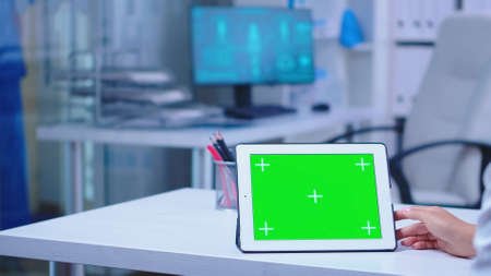 Close up of doctor using tablet computer with green chroma key in hospital cabinet. Doctor in health clinic working on tablet computer with replaceable screen doing medicine research.の写真素材