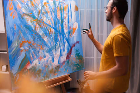 Young artist standing in front of painting in art workshop. Painting a masterpiece. Modern artwork...