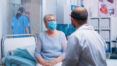 Old retired senior woman wearing a mask at doctor consultation during COVID-19 pandemic. Healthcare system, disease treatment in modern professional private clinic or hospitalの写真素材