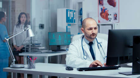 Happy medical staff smiling to camera. Practitioner doctor working on PC while medical staff and...