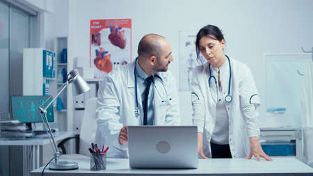 Male and female doctor practitioners consulting each other over a medical problem regarding a patient. Authentic modern private hospital clinic room healthcare system medicine and treatmentの写真素材