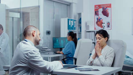 Young woman receiving devastating news from doctor about her health, she starts crying and feels lost, sad, depressed. Cancer or other terminal ill conceptの写真素材