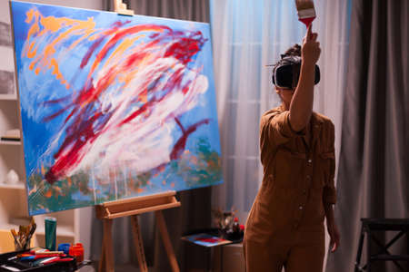 Talented painter with vr headset painting a masterpiece on canvas in art studio. Modern artwork paint on canvas, creative, contemporary and successful fine art artist drawing masterpieceの写真素材