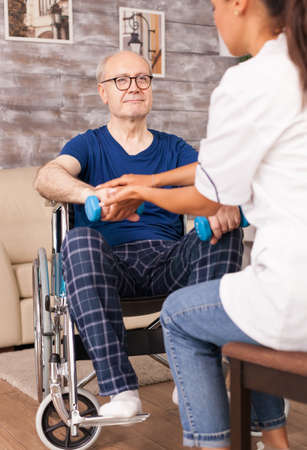 Senior man trying to raise his hand using dumbbells. Disabled handicapped old person with social...