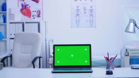 Laptop in hospital cabinet with green screen and nurse wearing blue uniform holding protection mask. Notebook with replaceable screen in medic clinic.の写真素材