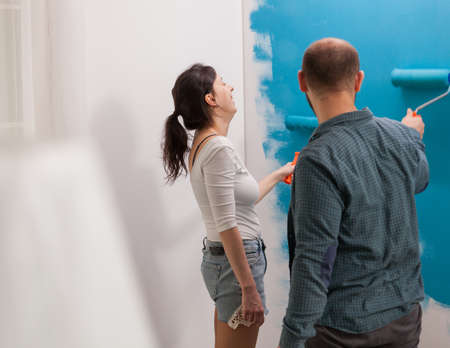 Young family having fun painting the apartment wall with strong color. Home during renovation,...