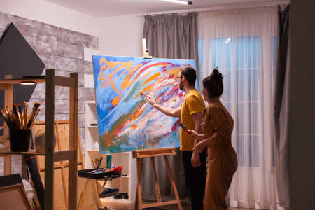 Couple working together on masterpiece painting on art workshop. Modern artwork paint on canvas, creative, contemporary and successful fine art artist drawing masterpieceの写真素材