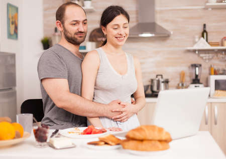 Couple doing online shopping on laptop during breakfast. Entering information, customer using...