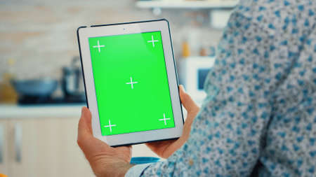 Grandgather using tablet pc with green screen in kitchen while enjoying his breakfast. Elderly...