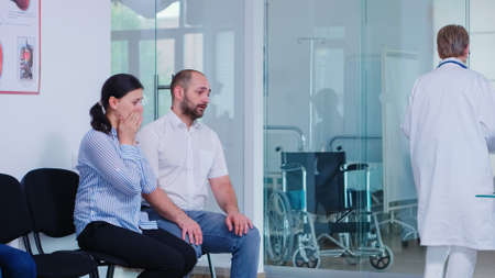 Young wife crying after hearing doctor bad news in hospital waiting room. Doctor giving unfavorable test results. Stressed man and woman during medic appointment.の写真素材