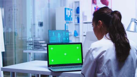 Health practitioner using laptop with chroma key in private clinic wearing white coat while nurse in blue uniform checking patient results on computer.の写真素材