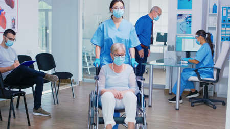 Senior man discussing with nurse at hospital reception wearing mask against coronavirus, assistant...