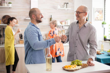 Happy son and father clinking wine glasses in kitchen during lunch with family.の写真素材