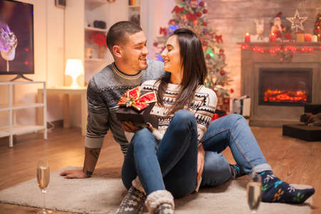 Loving couple with magic gift box celebrating christmas. Warm fireplace.の写真素材