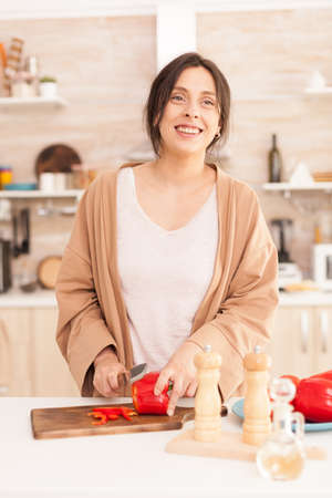 Smiling woman chopping food ingrediend in kitchen. Wife cutting red bell pepper. Beautiful cheerful...