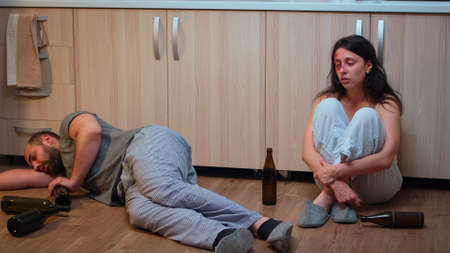 Helpless beaten woman suffering sitting on the floor near drunk man. Alcoholic aggressive husband...