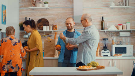 Extended family putting the groceries in the fridge. Young couple coming from shopping bringing a paper bag with groceries, fresh food from supermarket at parents home to prepare family dinnerの写真素材