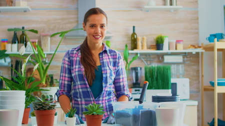 Florist woman looking at camera and smiling surrounded by flowers. Using fertil soil with a shovel, white ceramic pot and houseflower, plants, prepared for replanting for house decoration.の写真素材