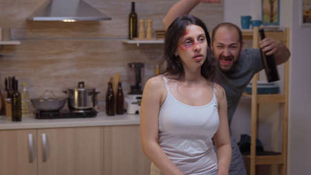 Wife abused by an alcoholic husband being a victim of violence. Violent aggressive man injuring terrified helpless, vulnerable, afraid, beaten panicked woman living in terror pressure and sufferingの写真素材