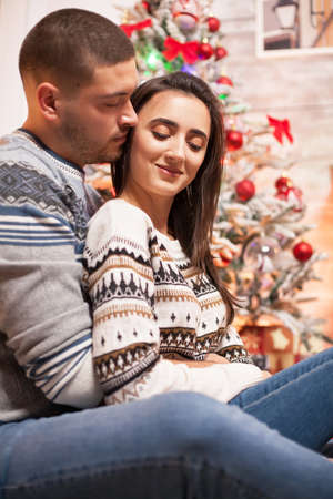 Happy girl while boyfriend is hugging her next to christmas tree.