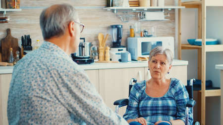 Handicapped senior woman in wheelchair bonding with husband while food is getting ready on gas...
