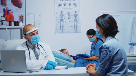 Nurse consulting child laying in bed wearing protection mask. Physician specialist in medicine...