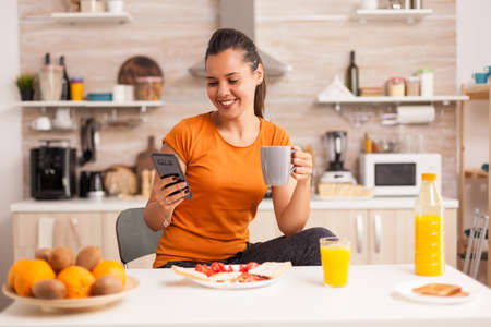 Woman drinking a cup of coffee while browsing on phone. Housewife using modern tehcnology and drinking healthy, natural, homemade coffee. Refreshing morningの写真素材
