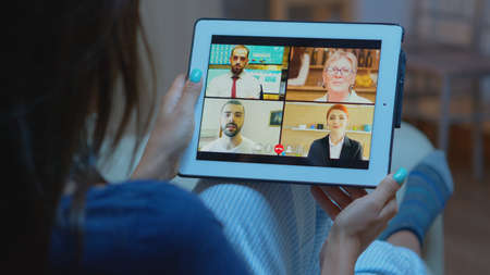 Woman listening online training on tablet late at night sitting on sofa. Remote worker having...