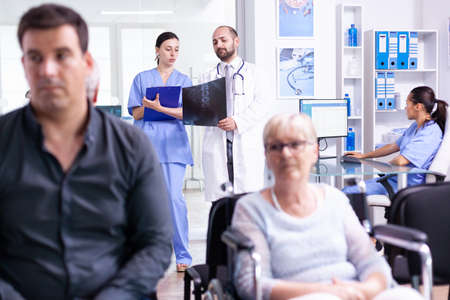 Nurse looking at radiography while talking with doctor about patient diagnosis in hospital waiting...