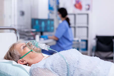 Senior woman breathing through oxygen mask after being infected with coronavirus and getting...
