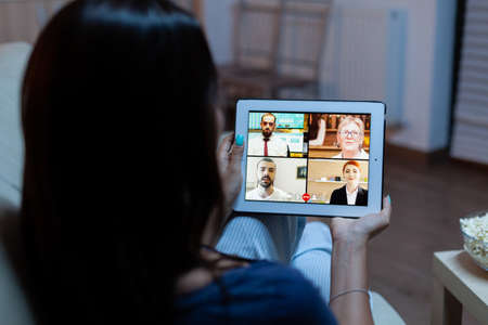Woman listening online training on tablet late at night sitting on sofa. Remote worker having...