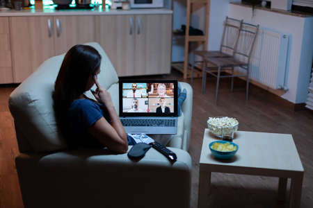 Woman speaking with colleagues on webcam lying on sofa at home. Remote worker having online meeting,...