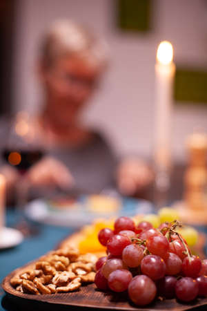 Nuts and grapes sitting on wooden plate during elderly couple festive dinner. Senior couple sitting...