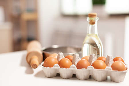 Pastry ingredients for homemade cakes and bread in empty kitchen. Modern dining room equipped with utensils ready for cooking with wheat flour in glass bowl and fresh eggs on tableの写真素材
