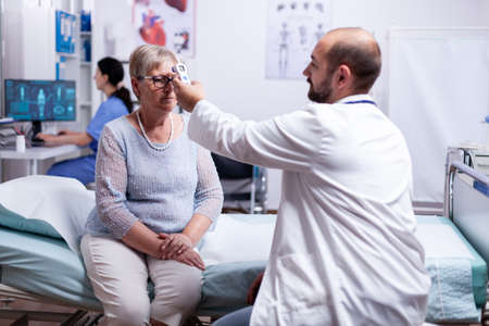 Medical staff using infrared thermometer to take old woman patient body temperature. Medical consultation for infections and disease during global pandemic,flu, tool, sickness.の写真素材