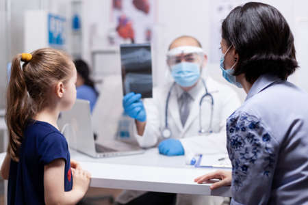 Mother with child at doctor consultation during coronavirus global pandemic. Pediatrician specialist with protection mask providing health care service radiographic treatment examinationの写真素材