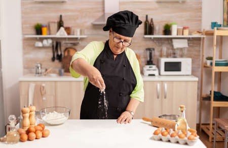 Preparation of delicious cookies in home kitchen by chef wearing apron. Happy elderly chef with...