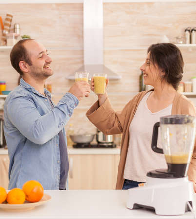 Couple holding nutritious smoothie in kitchen from tasty fruits. Healthy carefree and cheerful lifestyle, eating diet and preparing breakfast in cozy sunny morningの写真素材