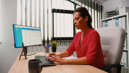 Hispanic young woman sitting in office and working on desktop pc. Entrepreneur sitting in front of...
