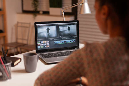 Brunette video editor works with footage on personal laptop in home ktichen during night time....