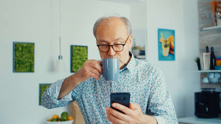 Happy grandfather listening music and dancing while having breakfast in kitchen wearing glasses...